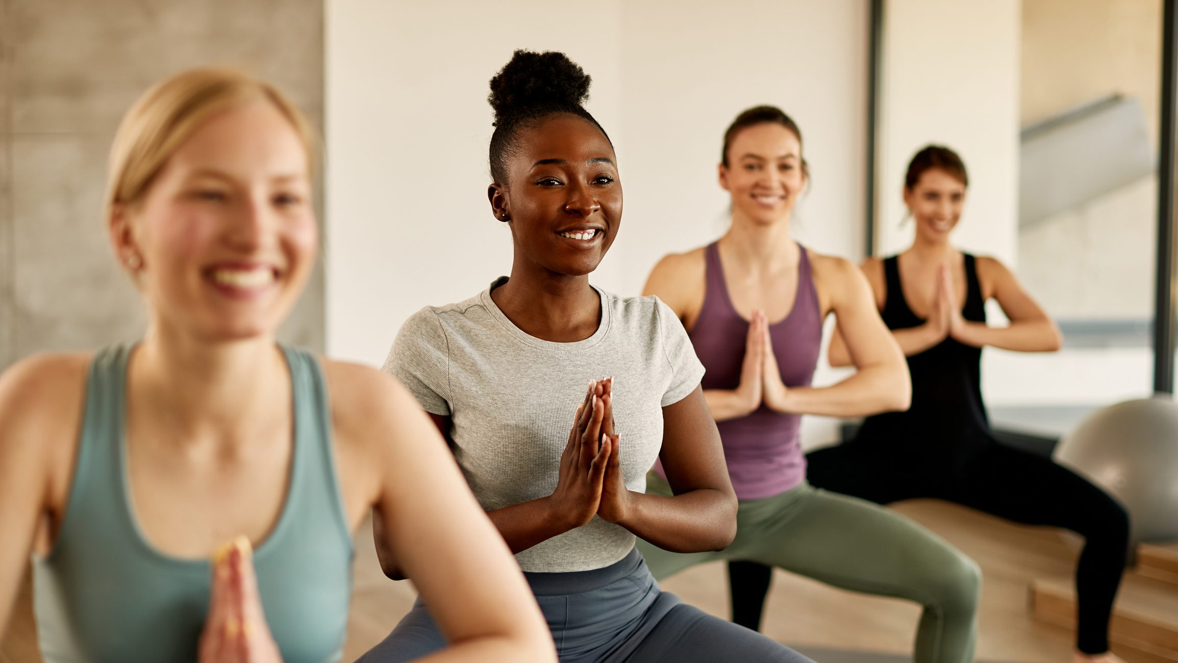Happy African American female athlete practicing Yoga with group of women at health club.